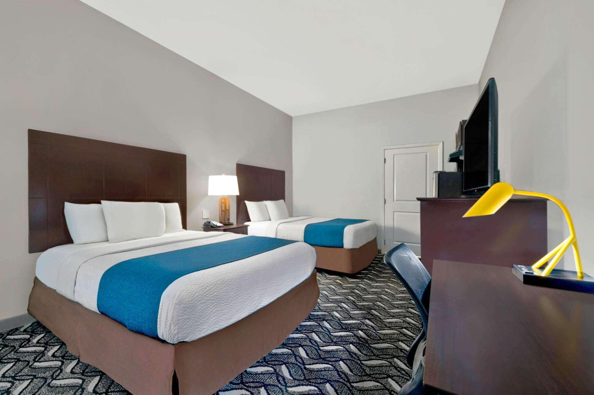 A hotel room with two beds, a desk, a television, and a lamp.