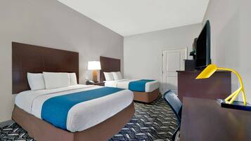 A hotel room with two beds, a desk, a television, and a lamp.