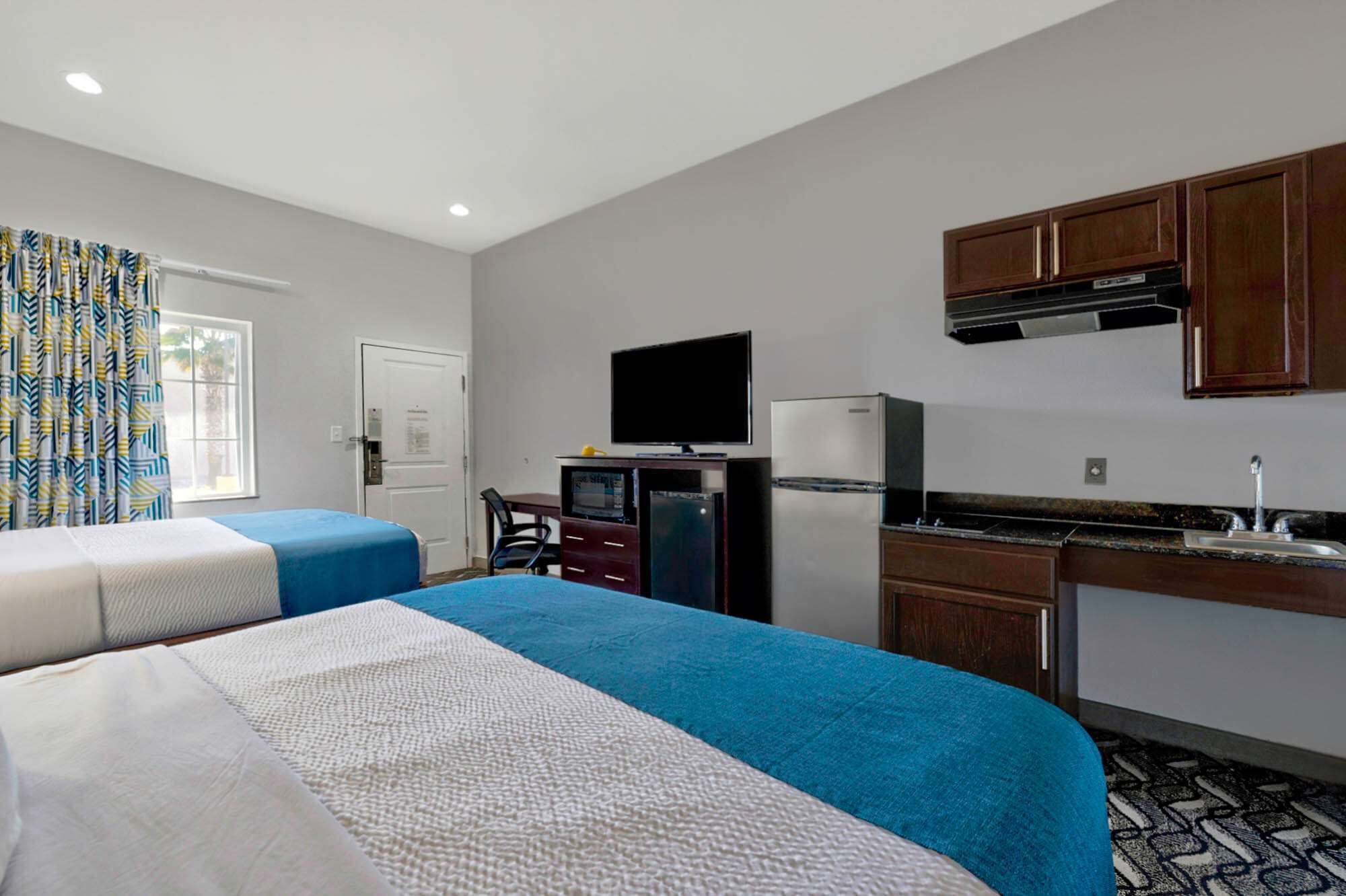 A hotel room with two beds, a desk with a computer, a television, a refrigerator, and a kitchenette.
