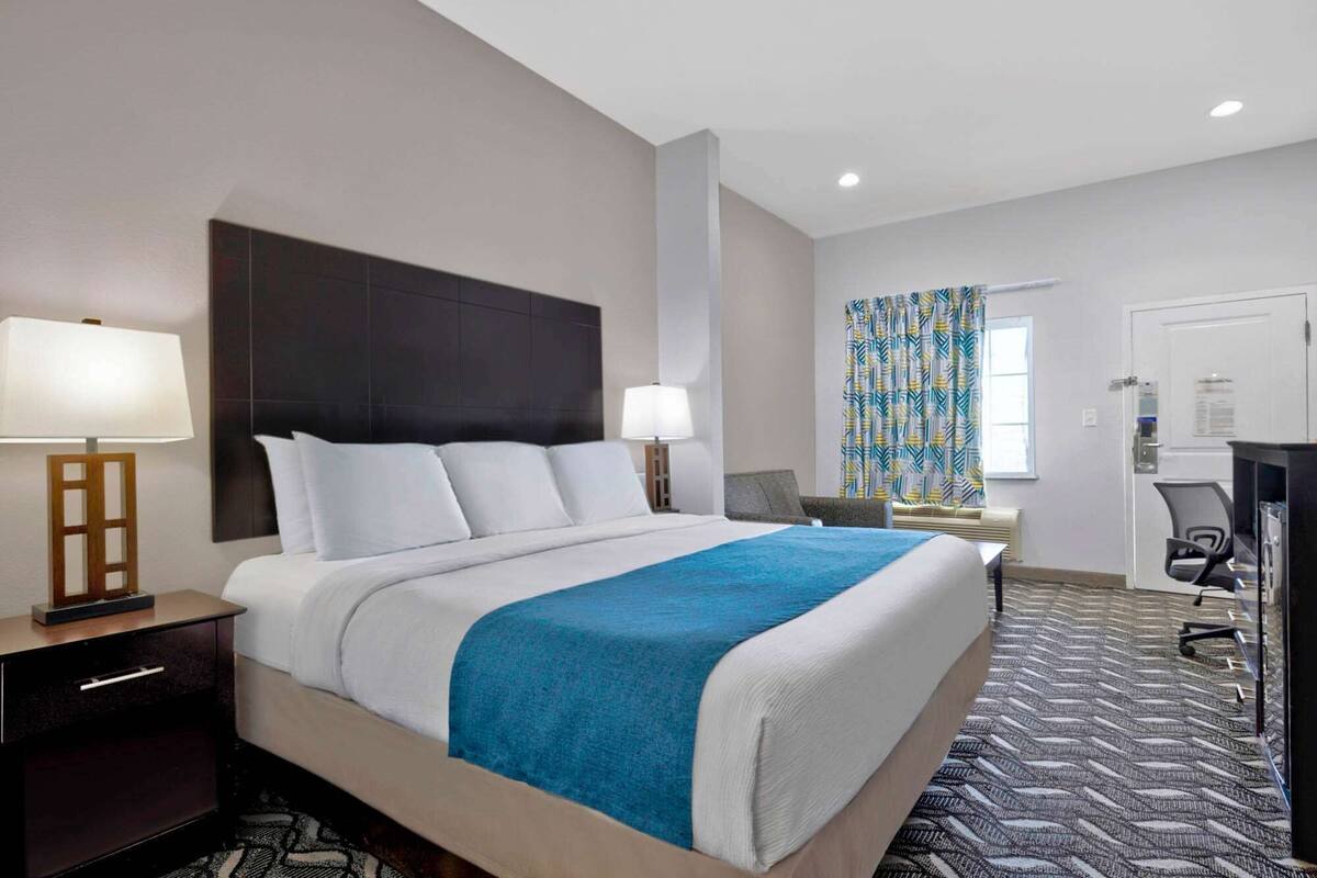 Habitación de hotel con una cama grande, dos mesitas de noche con lámparas, un escritorio con silla y una alfombra estampada.