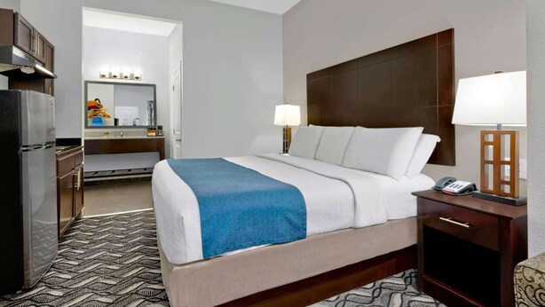 Ein Hotelzimmer mit Bett, Nachttisch, Lampe und Blick auf das Badezimmer.