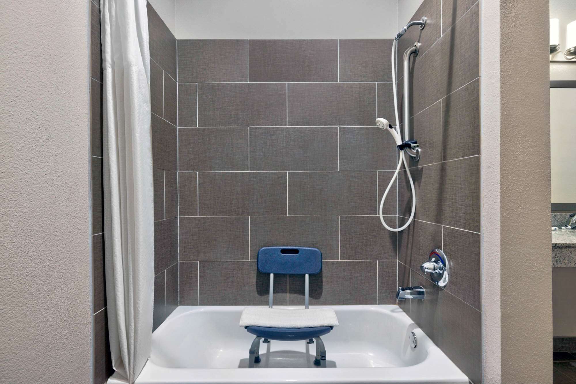 A bathroom with a white bathtub, a blue shower seat, and a handheld showerhead.