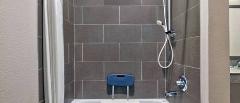 A bathroom with a white bathtub, a blue shower seat, and a handheld showerhead.