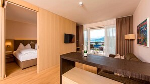 A modern hotel room with a bed, a desk, a flat-screen TV, and a balcony with a view. -  feel good Resort Wörthersee (Krumpendorf am Woerther See)
