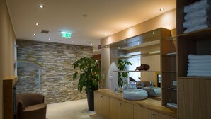 A modern bathroom with a stone wall, a large mirror, wooden cabinets, and a plant. -  feel good Resort Wörthersee (Krumpendorf am Woerther See)