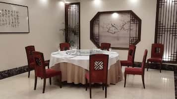 A round dining table with a white tablecloth, surrounded by six red chairs with patterned backrests, in a room with traditional decor and artwork on the walls.