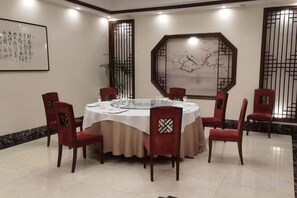 A round dining table with a white tablecloth, surrounded by six red chairs with patterned backrests, in a room with traditional decor and artwork on the walls. - Sihai Grand Hotel (Anshan)