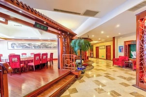 A hotel lobby with a dining area, a reception desk, and a staircase leading to the upper floor.