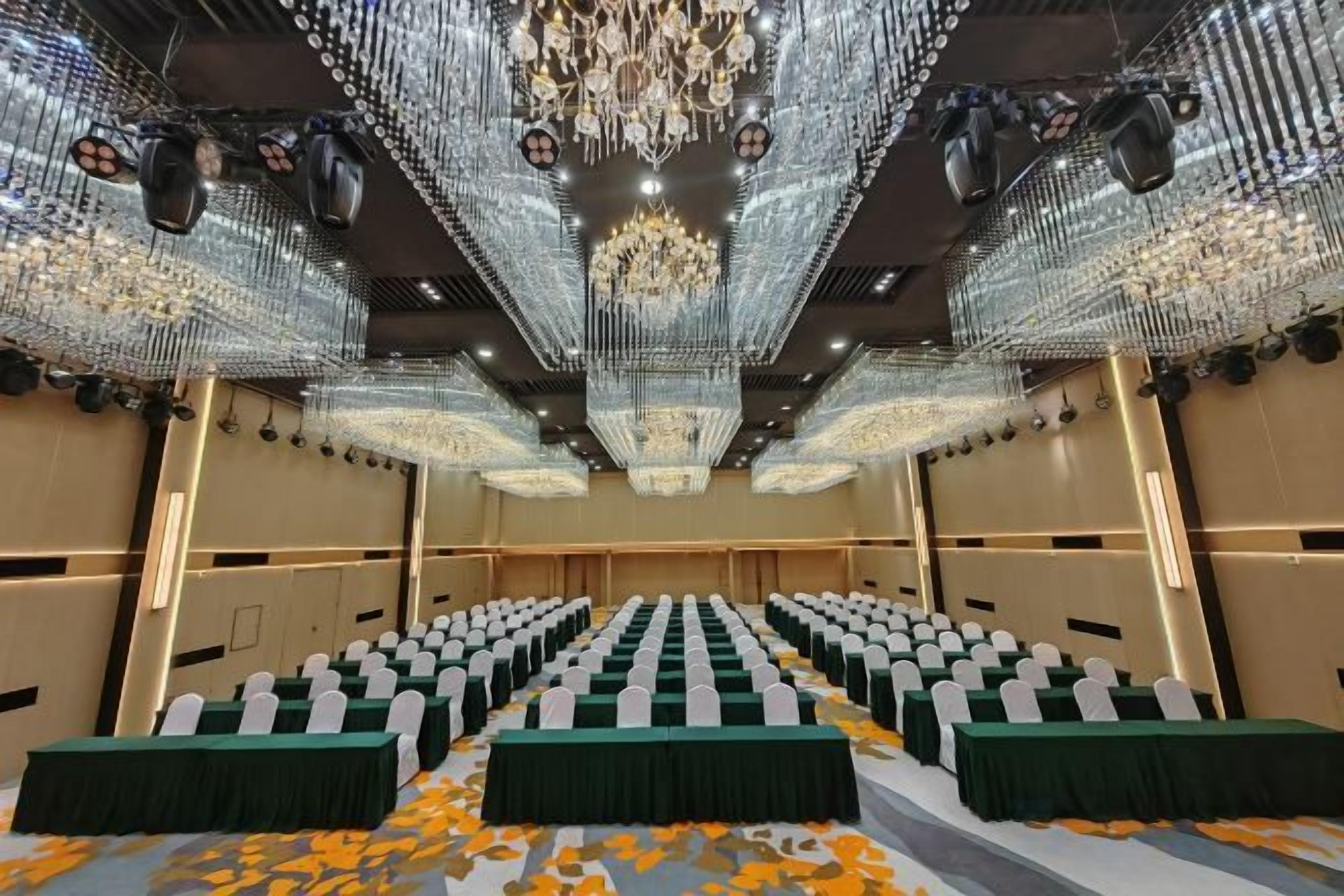 A conference room with rows of tables, a chandelier, and a carpet with a floral pattern.