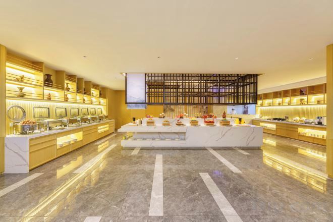 Vestíbulo de hotel con suelo de mármol, una recepción central y una zona de buffet con diversas opciones de comida.