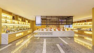 Vestíbulo de hotel con suelo de mármol, una recepción central y una zona de buffet con diversas opciones de comida.