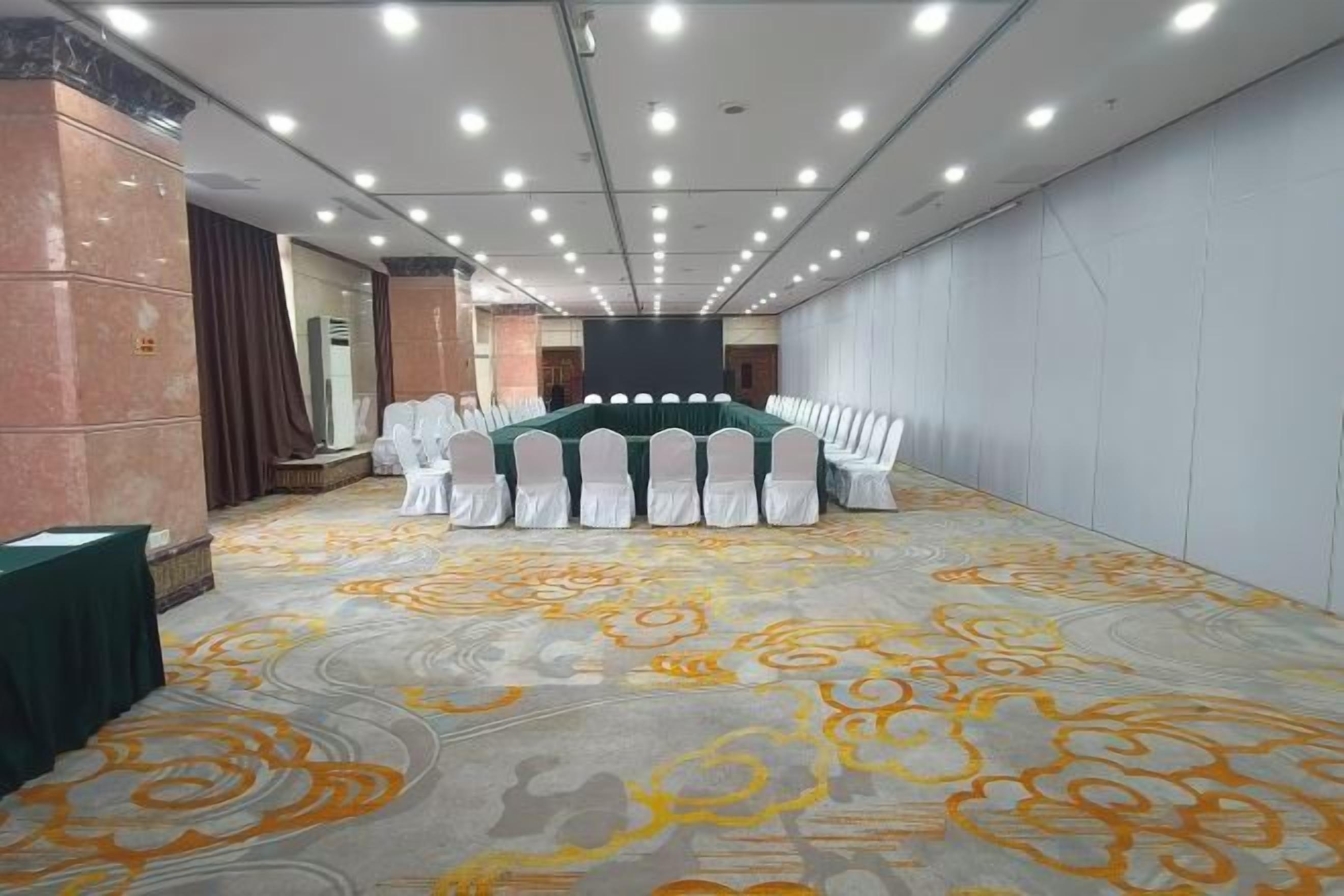 A conference room with a long table, white chairs, and a patterned carpet.