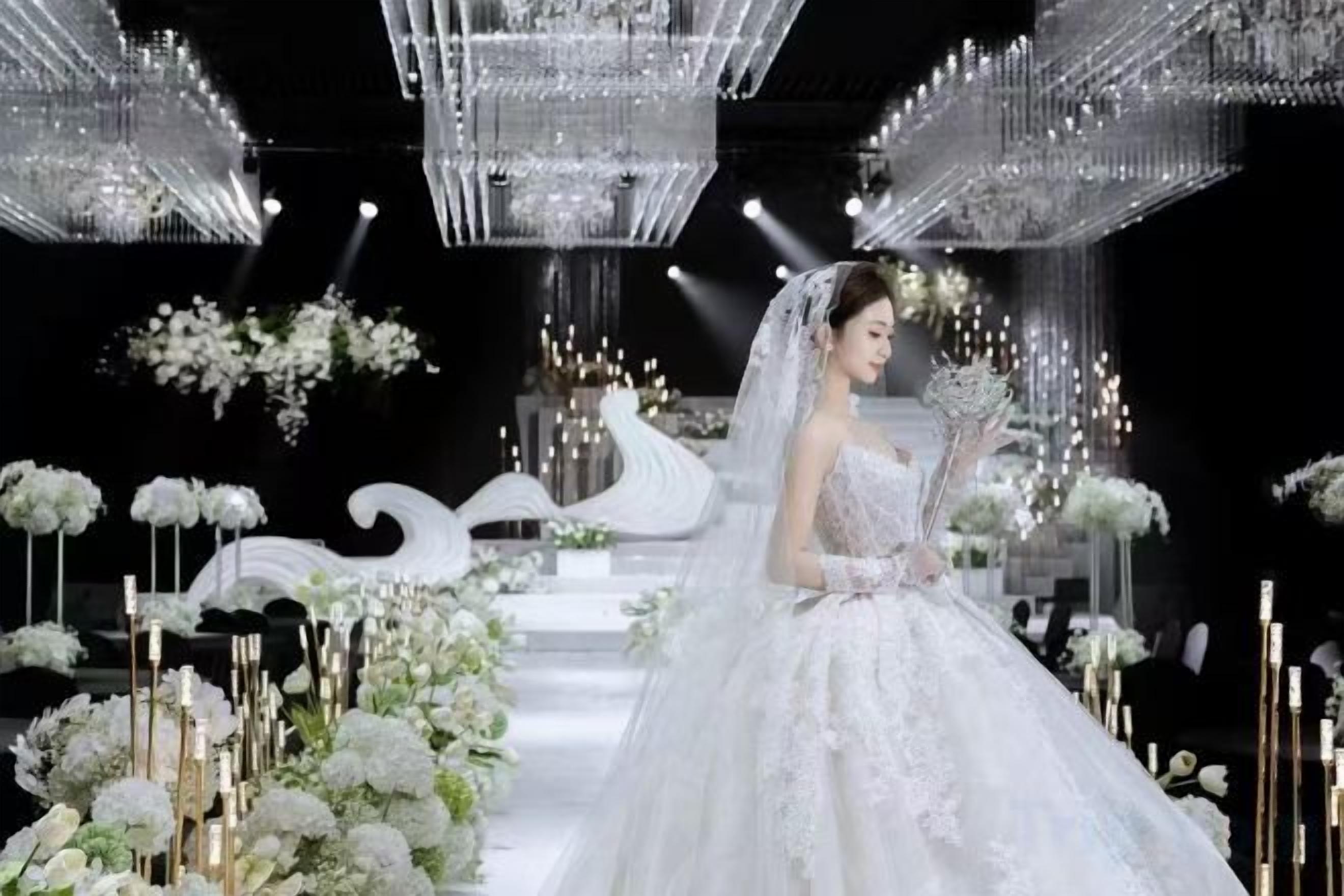 A wedding venue with a white aisle, floral decorations, and hanging chandeliers.