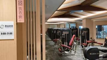 A gym with exercise equipment, a sign indicating operating hours, and a wooden partition.