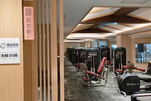 Un gimnasio con equipo de ejercicio, un cartel con los horarios de atención y una partición de madera.