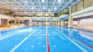 Ein großer, überdachter Pool mit deutlichen Bahnen, umgeben von einem mehrstöckigen Atrium mit Balkonen und Zimmerpflanzen.