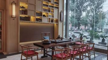 Une bibliothèque avec des étagères, un espace de lecture avec des fauteuils et une grande fenêtre donnant sur des arbres et des voitures.