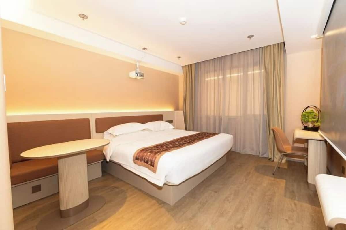 A modern hotel room with a bed, bedside table, seating area, and a small desk with a chair.