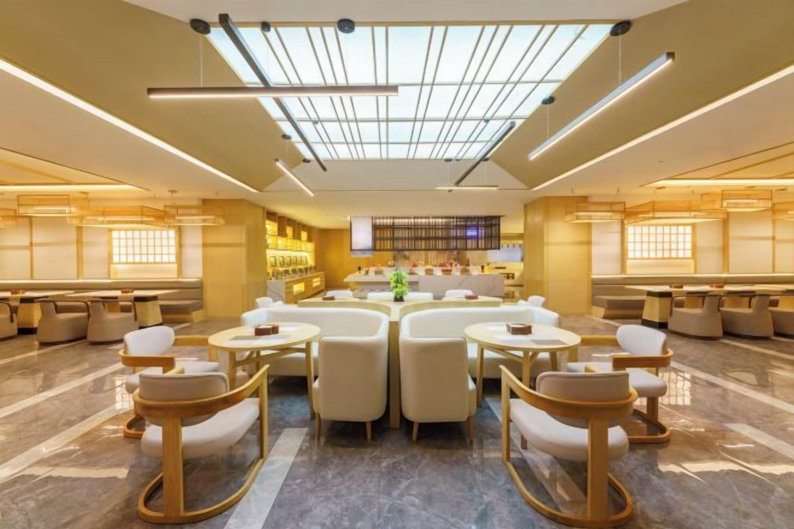 A spacious lobby with a high ceiling, a central seating area with round tables and chairs, and a bar area with shelves of bottles.
