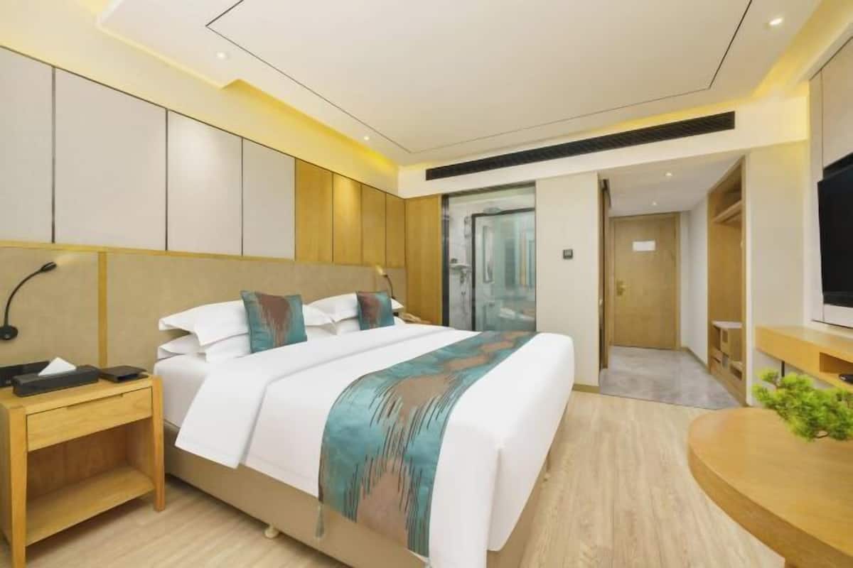 A modern hotel room with a large bed, bedside table, and a TV on a wooden stand.