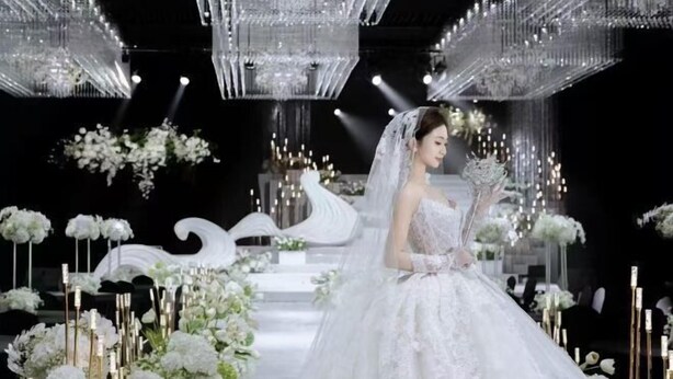 Ein Hochzeitssaal mit Kronleuchtern, Blumendekorationen und einer Braut in einem weißen Kleid.