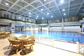 An indoor swimming pool with a tiled floor, surrounded by wicker chairs and a railing. - Sihai Grand Hotel (Anshan)