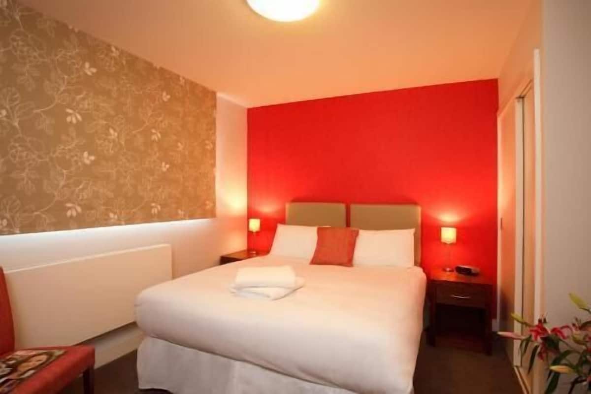 A hotel room with a bed, nightstands, and a red accent wall.
