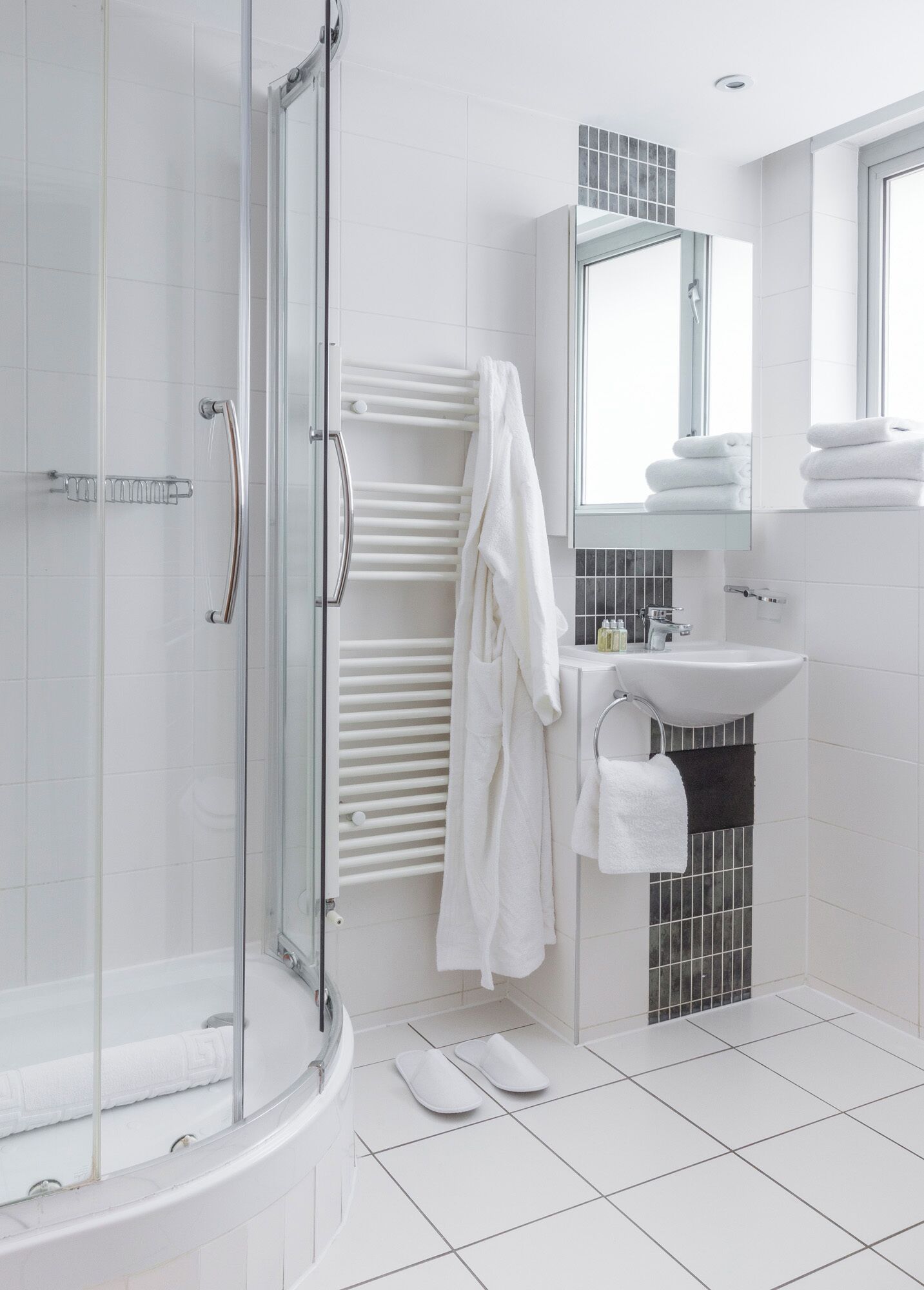 A modern bathroom with a glass shower enclosure, a white bathtub, a sink with a mirror above it, and a towel rack with folded towels.