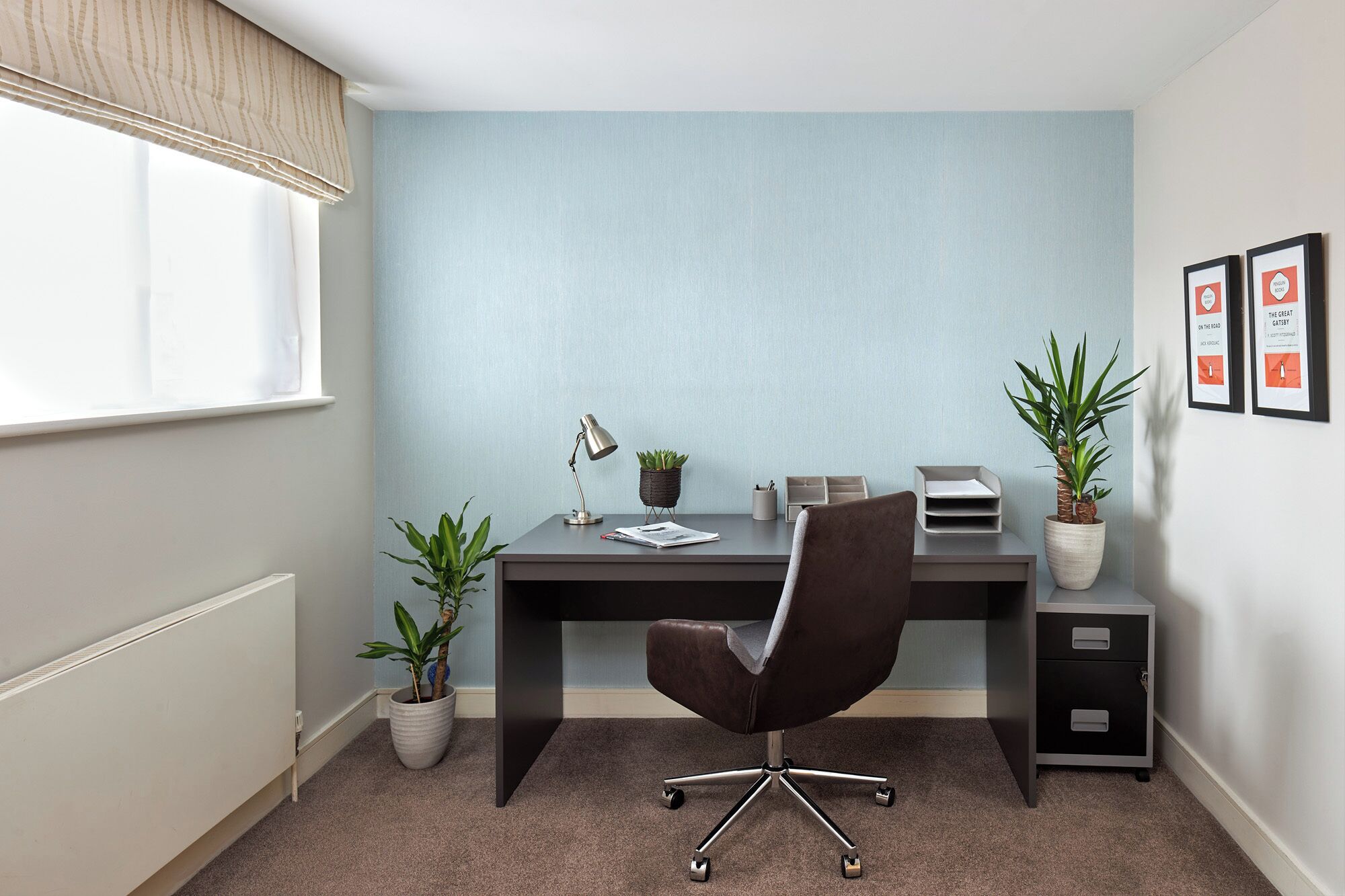 Ein moderner Büroraum mit Schreibtisch, Stuhl, Topfpflanzen und gerahmten Bildern an der Wand.
