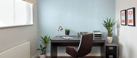 A modern office space with a desk, chair, potted plants, and framed pictures on the wall.