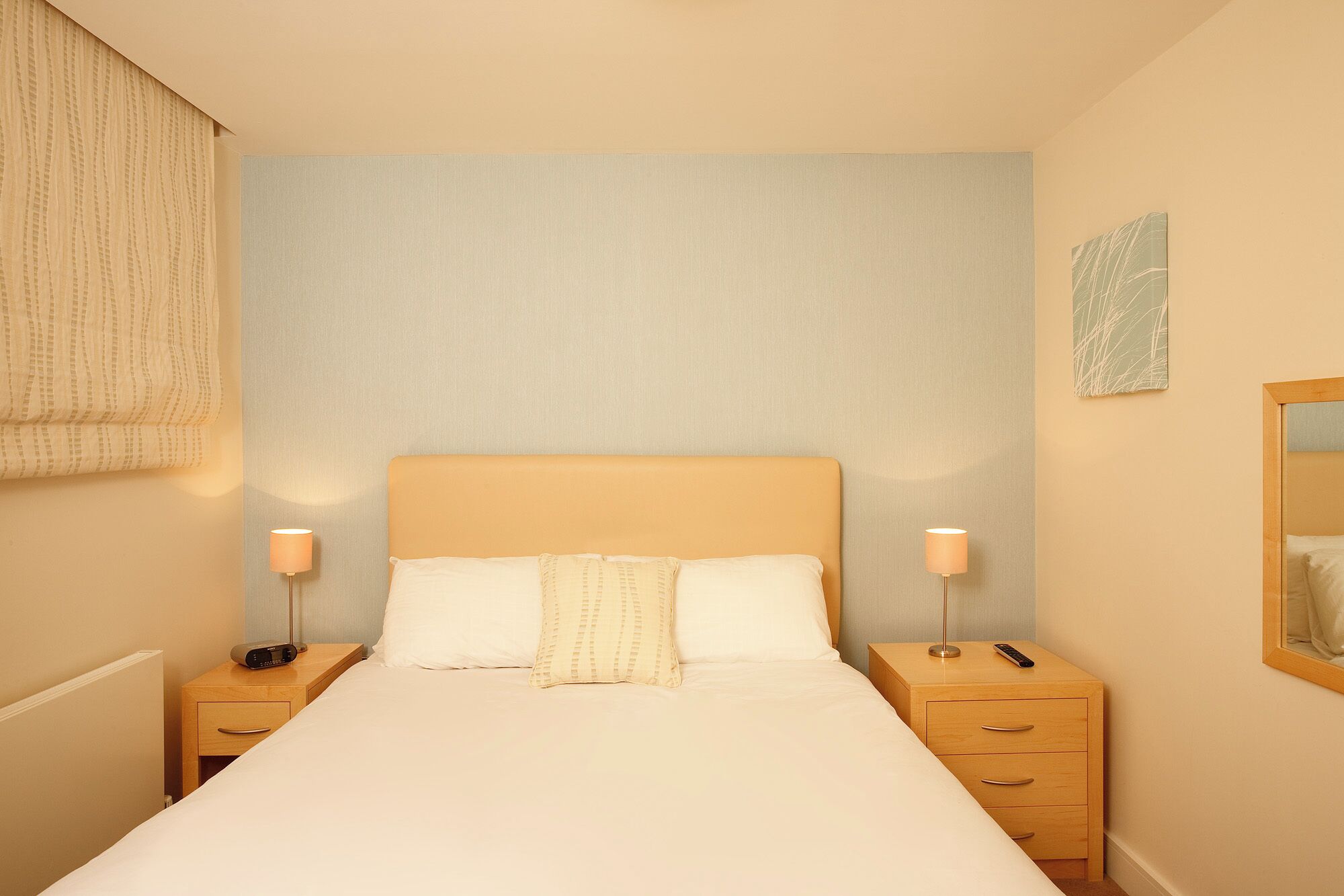 A hotel room with a bed, bedside tables, lamps, and a painting on the wall.