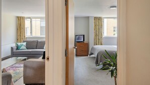 A hotel room with a sofa, a television on a wooden cabinet, a bed, and a potted plant. - SACO Holborn - Lamb's Conduit Street (London)