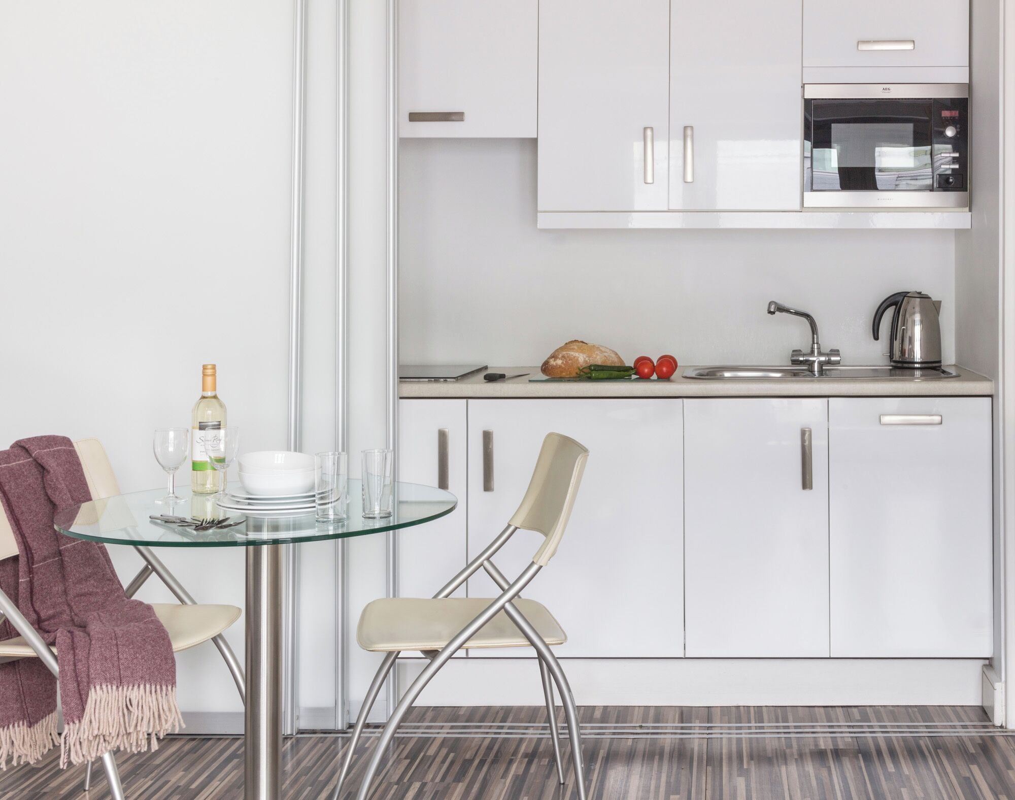 A modern kitchen with white cabinets, a microwave, and a kettle on the countertop.