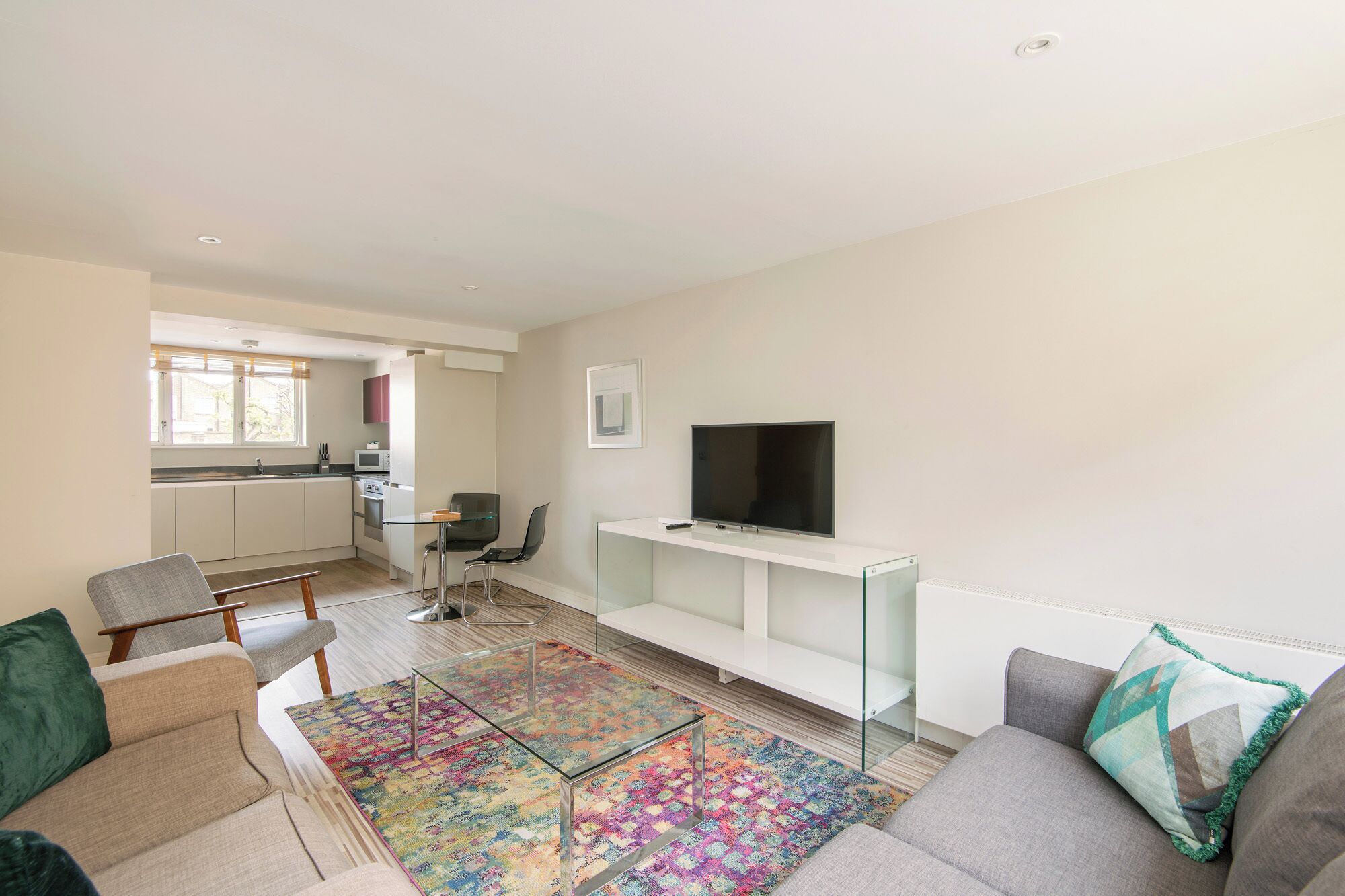 A modern living room with a sofa, a coffee table, a TV on a stand, and a kitchen in the background.