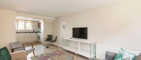 A modern living room with a sofa, a coffee table, a TV on a stand, and a kitchen in the background.