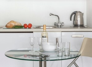 Una cocina con mesa de vidrio, botella de vino, copas y tetera.