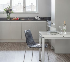 A modern kitchen with a dining area, a window with a view of buildings, and a vase with flowers on the counter. - SACO Holborn - Lamb's Conduit Street (London)