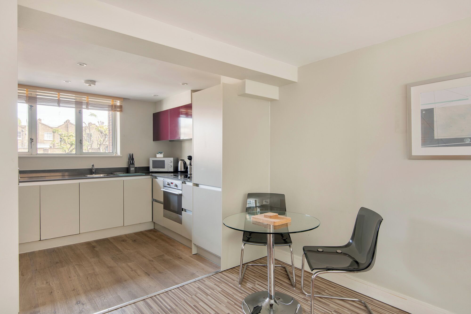 A compact kitchen with a microwave, kettle, and a small dining area with a glass table and two chairs.
