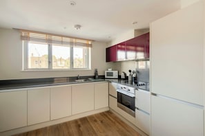 A modern kitchen with white cabinets, a stainless steel range, and a window with blinds. - SACO Holborn - Lamb's Conduit Street (London)