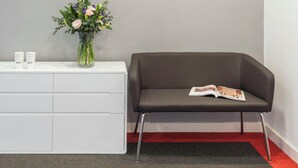 A reception area with two clocks labeled 'LONDON' and 'AMSTERDAM,' a vase with flowers, a white console table, and a brown leather sofa with a magazine. - SACO Holborn - Lamb's Conduit Street (London)