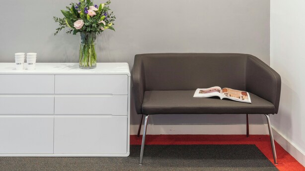 A reception area with two clocks labeled 'LONDON' and 'AMSTERDAM,' a vase with flowers, a white console table, and a brown leather sofa with a magazine. - SACO Holborn - Lamb's Conduit Street (London)