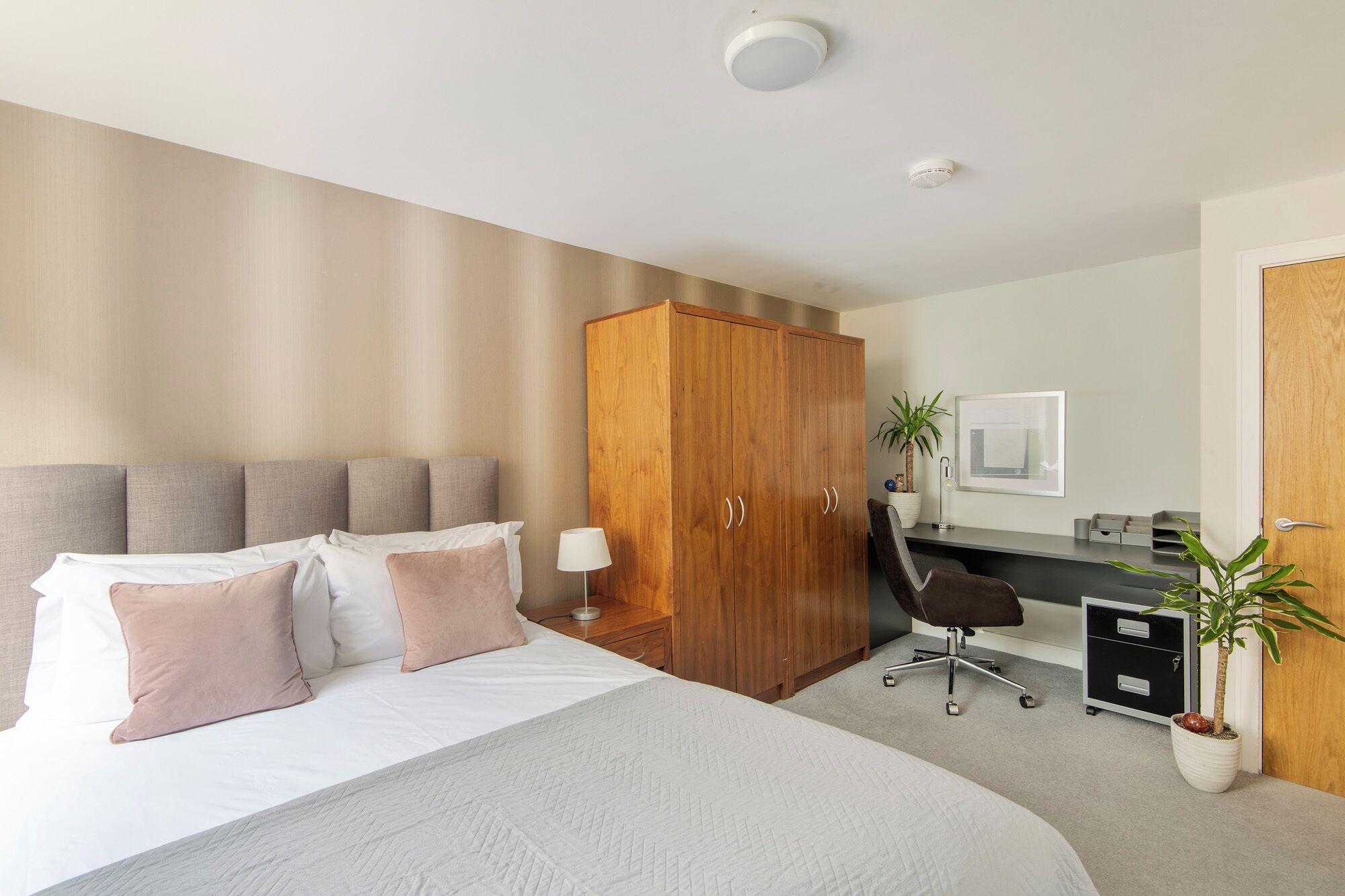 A hotel room with a bed, a desk, a wardrobe, and a chair.