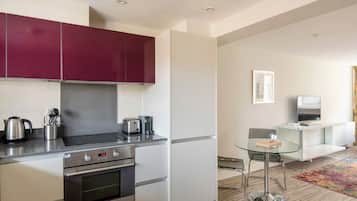A modern kitchen with stainless steel appliances, a glass dining table, and a minimalist living area with a flat-screen TV.
