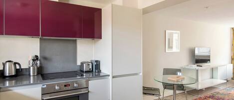 A modern kitchen with stainless steel appliances, a glass dining table, and a minimalist living area with a flat-screen TV.