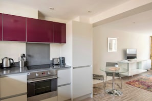 A modern kitchen with stainless steel appliances, a glass dining table, and a minimalist living area with a flat-screen TV. - SACO Holborn - Lamb's Conduit Street (London)