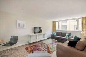 A modern living room with a glass coffee table, a sofa, a television, and a window with curtains. - SACO Holborn - Lamb's Conduit Street (London)