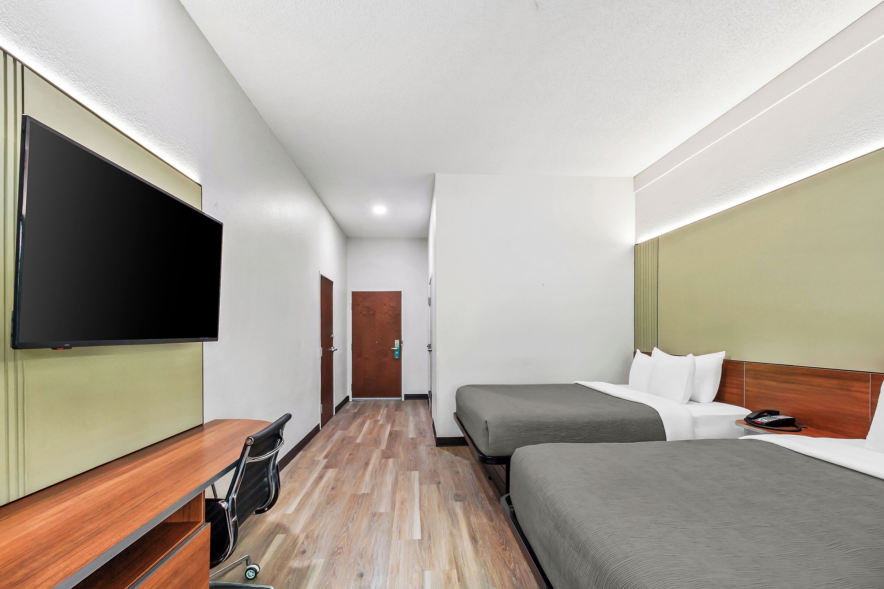 A hotel room with a flat-screen TV, a desk with a chair, two beds, and a wooden floor.
