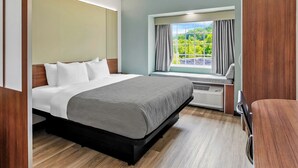 A modern hotel room with a large bed, a window with curtains, a built-in heater, and a wooden desk.