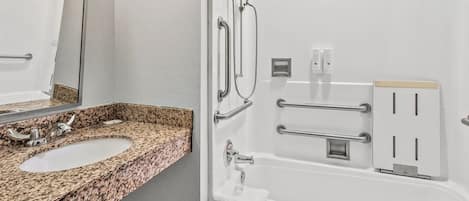 A bathroom with a granite countertop sink, a mirror, a shower with grab bars, and a towel rack.