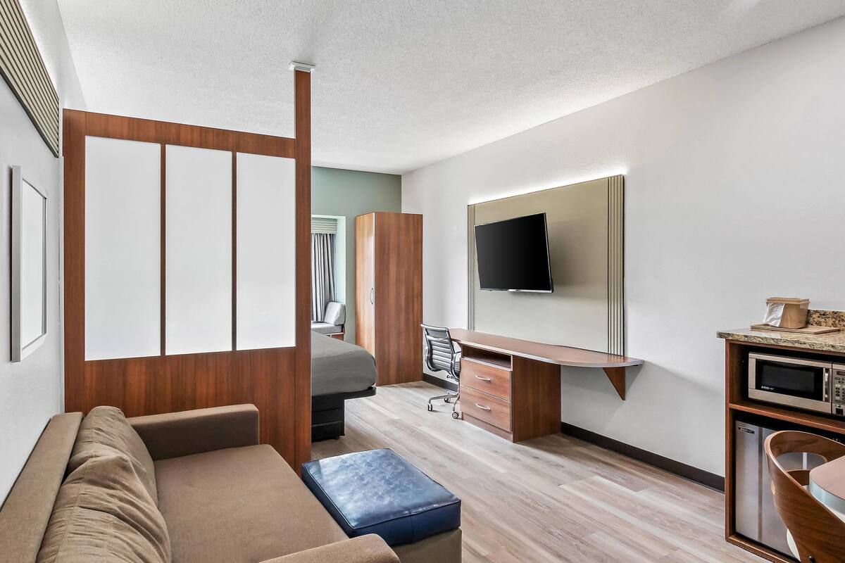 A modern hotel room with a sofa, a desk, a television, and a microwave.